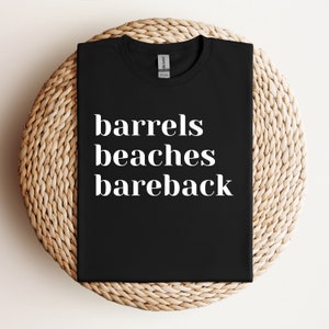 Puede incluir: Camiseta negra con texto blanco que dice "barrels beaches bareback".