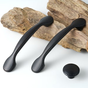 May include: Two black cabinet pulls with a decorative stitched design and a matching black knob.