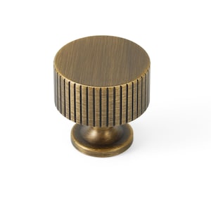 May include: A round, antique brass cabinet knob with a fluted design. The knob has a smooth, brushed finish.