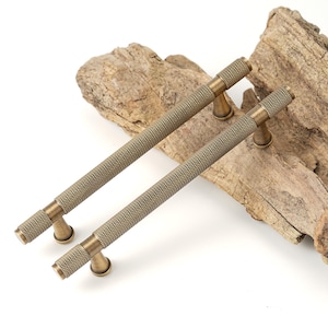 May include: Two antique brass cabinet pulls with a textured, ridged design. The pulls are approximately 6 inches long and have a slightly tapered shape.
