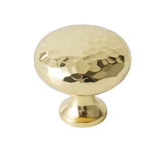 May include: A gold hammered metal cabinet knob with a round top and a short, round base.