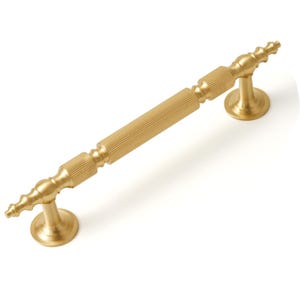 May include: A gold-toned cabinet pull with a fluted design and rounded ends. The pull is approximately 6 inches long.