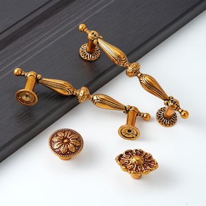 May include: Four ornate gold-toned cabinet knobs and pulls with intricate floral designs. The knobs are round and the pulls are long and narrow.