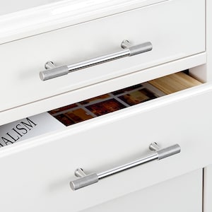 May include: Two white drawers with silver cabinet pulls. The top drawer is open and has a magazine with the word "ALISM" visible. The bottom drawer is closed.