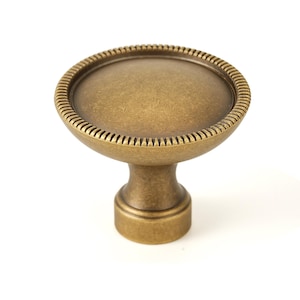 May include: A round, antique brass cabinet knob with a decorative, beaded edge and a slightly domed top.