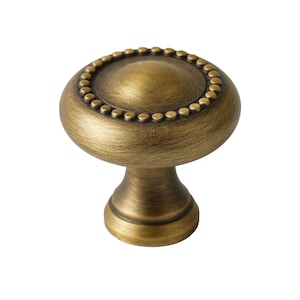 May include: A round, antique brass cabinet knob with a beaded edge and a slightly domed top.