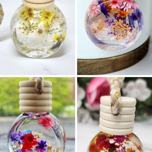 May include: Four clear glass car air fresheners filled with dried flowers. Each bottle has a wooden cap and a braided rope. The flowers are in shades of yellow, red, purple, and pink. The bottles are approximately 5 cm in diameter.