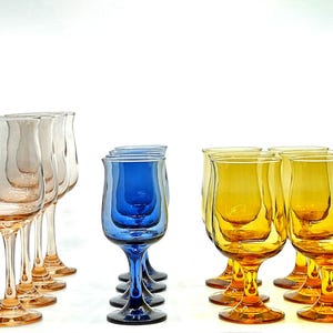 Op de afbeelding: Een verzameling gekleurde wijnglazen. De glazen zijn gegroepeerd in tinten roze, blauw en geel. De glazen hebben een uniek, gebogen ontwerp en staan tegen een witte achtergrond.