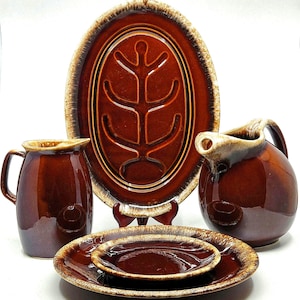 May include: A vintage brown ceramic serving set with a glossy finish. The set includes an oval platter with a tree design, a pitcher, a creamer, and two plates. The edges have a lighter brown trim.