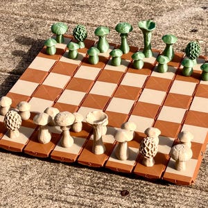 Op de afbeelding: Een uniek schaakspel met paddenstoelvormige stukken in groen en cr&egrave;me. Het bord heeft een bruin en cr&egrave;me geblokt patroon. De stukken zijn ingewikkeld ontworpen en geven een grillige toets aan het klassieke spel.
