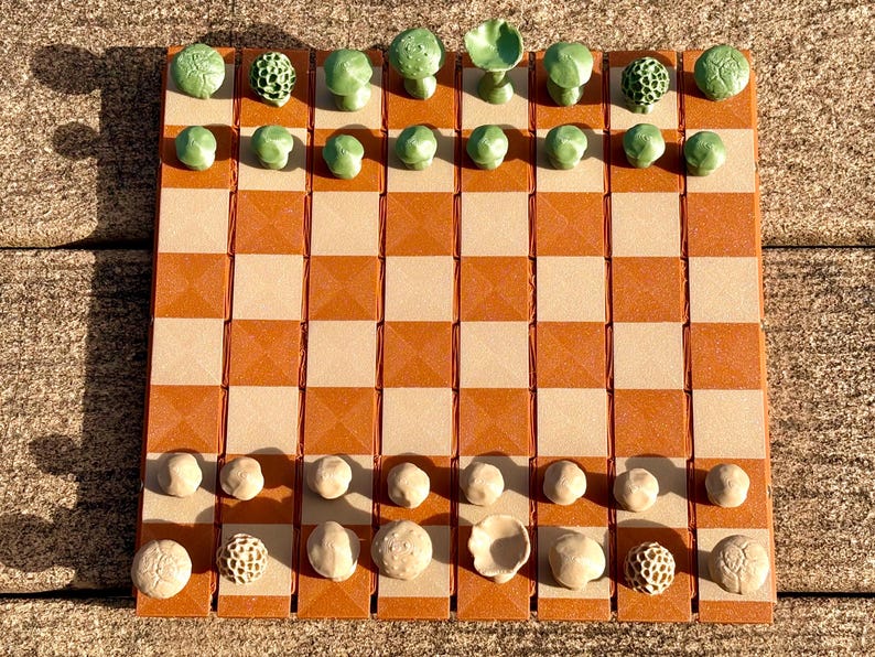Op de afbeelding: Een unieke schaakset met een bruin en beige geblokt bord. De schaakstukken zijn groen paddenstoelvormig en beige, wat een grillige toets toevoegt aan het klassieke spel. Het bord meet ongeveer 30 cm bij 30 cm.