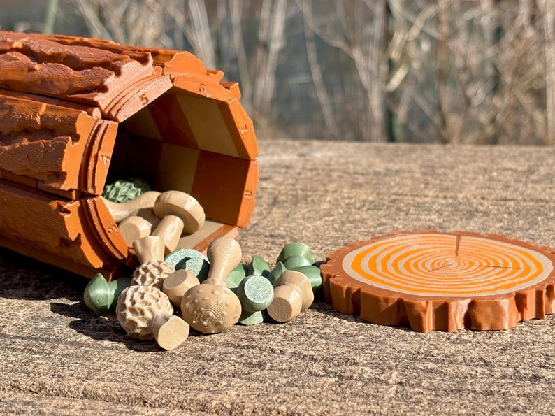 Op de afbeelding: Een houten speelgoedset met een holle boomstam met een dambordinterieur, waaruit verschillende paddenstoelvormige stukken vallen. Een apart, rond houten stuk lijkt op een schijf van een boom. De set is in tinten bruin, beige en groen.