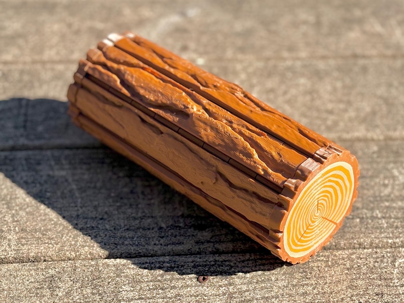 Op de afbeelding: Een decoratieve log-vormige doos met een gedetailleerde houtnerftextuur. De uiteinden van de log hebben concentrische cirkels en de algehele kleur is een warm bruin met lichtere accenten. De doos is ontworpen om op een realistische log te lijken.