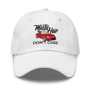 Puede incluir: Gorra de béisbol blanca con el texto bordado "Miata Hair Don't Care" y un gráfico de un coche rojo.
