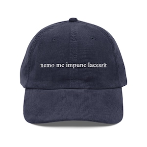 May include: A navy blue corduroy baseball cap with white embroidered text that reads "nemo me impune lacessit".