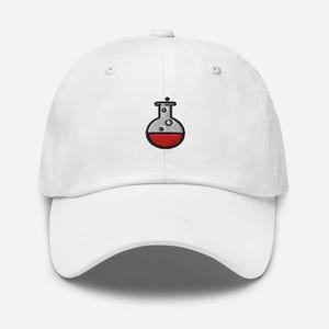 May include: White baseball cap with a red and black embroidered flask design. The flask is filled with a red liquid and has bubbles at the top. The cap has a curved brim and an adjustable strap.