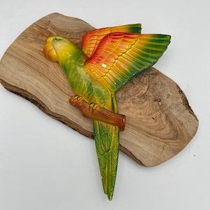 May include: A green, yellow, orange, and red parrot figurine with outstretched wings, perched on a branch. The figurine is made of ceramic and has a realistic appearance.