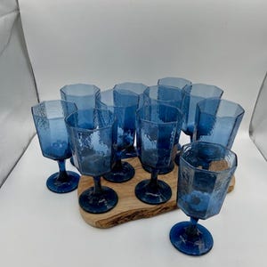 Puede incluir: Conjunto de diez copas de vino de vidrio azul con superficie texturizada. Las copas están dispuestas sobre una superficie de madera.
