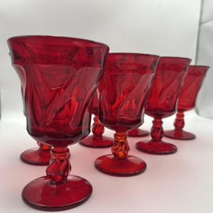 Può includere: Set di sei calici rossi rubino. Ogni bicchiere presenta un motivo decorativo a spirale sulla coppa e uno stelo a torsione. I bicchieri hanno un'estetica classica e vintage, perfetti per servire bevande.
