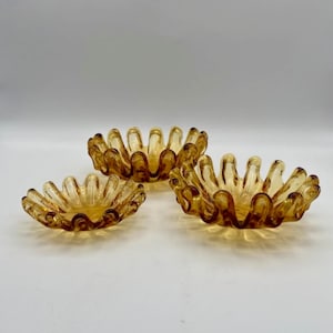 Puede incluir: Conjunto de tres cuencos de vidrio ámbar con un borde ondulado y fruncido. Los cuencos están anidados.