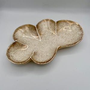 Op de afbeelding: Een witte keramische serveerschaal met een gespikkeld bruin glazuur. De schaal is gevormd als een wolk met drie afgeronde secties.