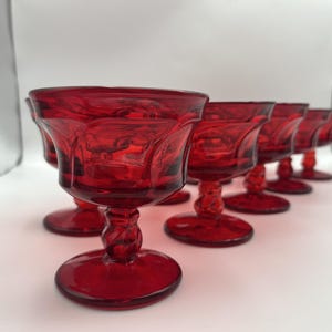 Peut inclure: Ensemble de six verres à pied rouge rubis. Chaque verre présente une coupe texturée et une tige torsadée. Les verres sont disposés en rangée, mettant en valeur leur design élégant et leur couleur vibrante.