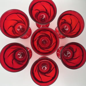 Puede incluir: Vista aérea de siete copas de cóctel rojas dispuestas en un patrón circular. Cada copa presenta un tono rojo vibrante con patrones oscuros y arremolinados. Los tallos y las bases también son rojos, creando un diseño elegante.
