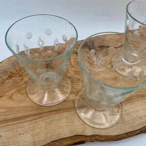 Puede incluir: Tres vasos de beber de vidrio transparente con un diseño grabado en blanco de puntos y diamantes sobre una superficie de madera.