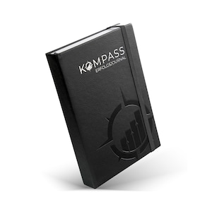 Könnte beinhalten: Schwarzes, ledergebundenes Journal mit einem Kompass-Design und dem geprägten Text "KOMPASS ERFOLGSJOURNAL" auf dem vorderen Umschlag.