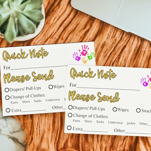 Puede incluir: Dos tarjetas crema "Quick Note" con diseños de huellas de manos coloridas. Las tarjetas tienen secciones para completar para los elementos "Please Send", como pañales, toallitas y ropa. Las tarjetas están sobre una superficie naranja texturizada.