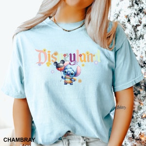 Puede incluir: Una camiseta azul claro con un gr&aacute;fico de "Disneyland" colorido que presenta a Stitch sosteniendo un globo de Mickey Mouse. El gr&aacute;fico tambi&eacute;n incluye flores y estrellas.