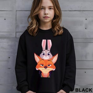 May include: Black sweatshirt featuring a graphic of Judy Hopps the bunny and Nick Wilde the fox from the animated movie Zootopia. The sweatshirt has a crew neck and long sleeves. The word "BLACK" is printed in white at the bottom right.