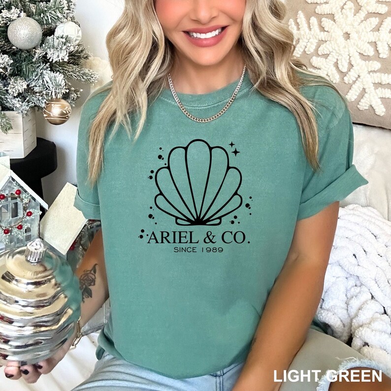 May include: A light green t-shirt with a black seashell graphic and the text "Ariel & Co. Since 1989".