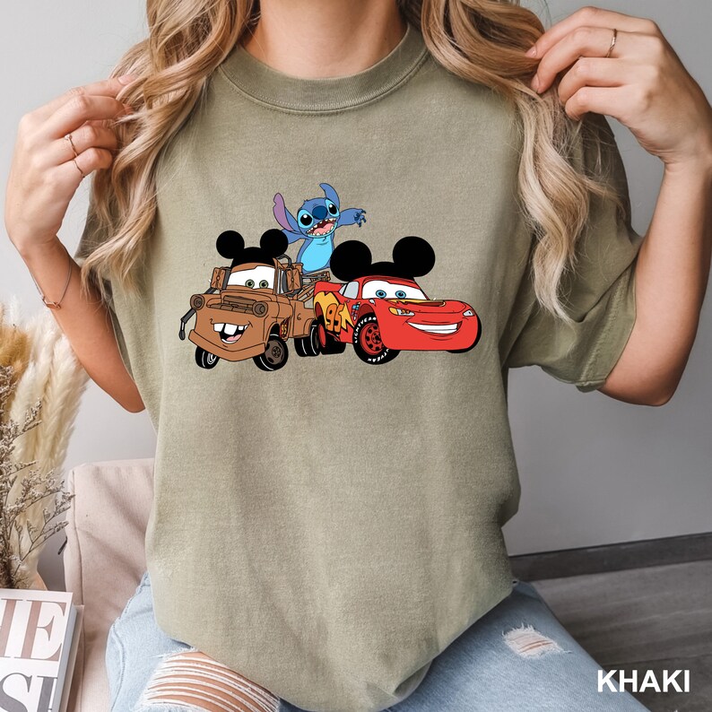 May include: Khaki t-shirt with a graphic print of Stitch from Lilo & Stitch, Mickey Mouse, and Lightning McQueen from Cars.