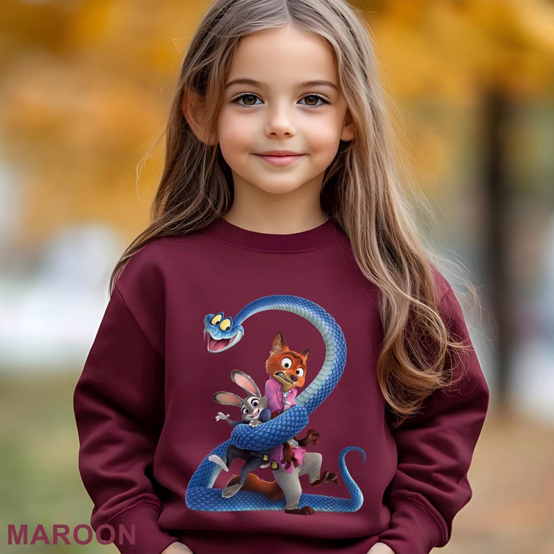 May include: Maroon sweatshirt featuring a cartoon image of a blue snake wrapped around a fox and a rabbit. The sweatshirt has long sleeves and a crew neck. The word "MAROON" is printed at the bottom.