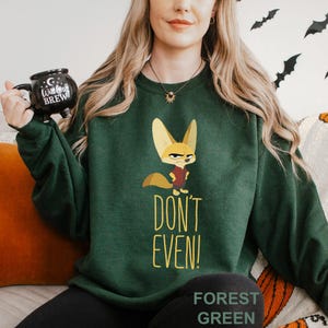 May include: A dark green sweatshirt with a cartoon fox and the words "DON'T EVEN!" in yellow. The sweatshirt has a crew neck and the text "FOREST GREEN" at the bottom. The image has a Halloween theme.