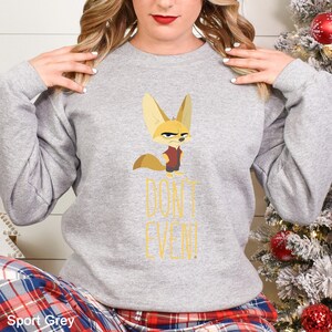 May include: Grey sweatshirt with a cartoon fennec fox wearing a red vest and a stern expression. The text "DON'T EVEN!" is printed in yellow. The sweatshirt is a casual style.