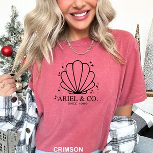 May include: A crimson red t-shirt with a black seashell graphic and the text "Ariel & Co. Since 1989".