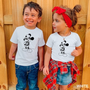 Może przedstawiać: Dwoje dzieci w białych koszulkach z czarno-białym obrazkiem Myszki Miki w okularach przeciwsłonecznych i czapce. Dziewczynka ma na sobie czerwoną kratkowaną sp&oacute;dniczkę i czerwoną opaskę na głowie. Chłopiec ma na sobie niebieskie dżinsy. Tekst "WHITE" jest widoczny w prawym dolnym rogu obrazu.