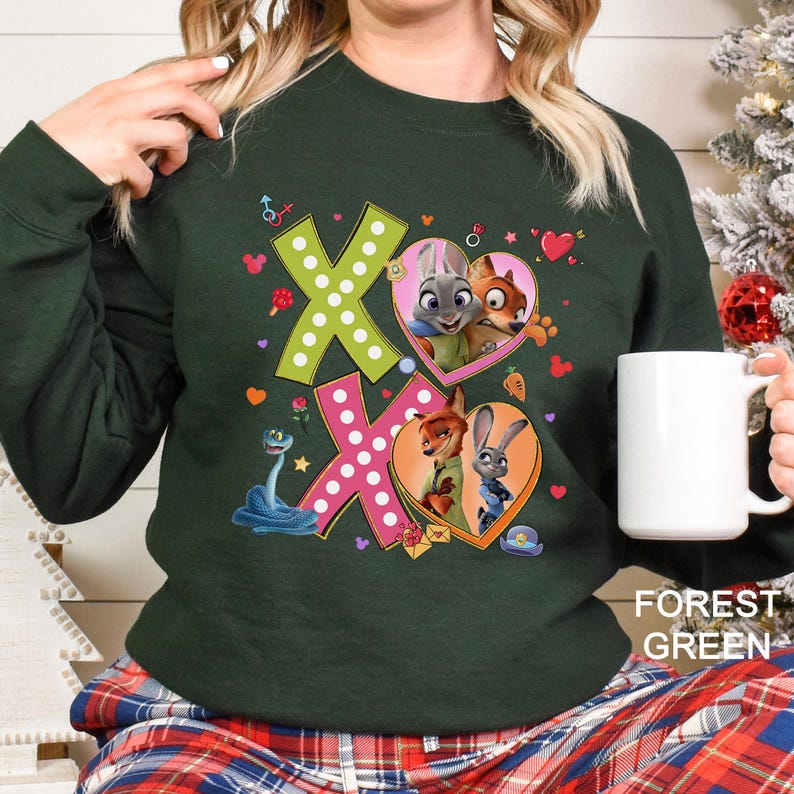 May include: Forest green sweatshirt featuring a colorful graphic of the characters from Zootopia. The design includes the letters "XO" with heart-shaped images of Judy Hopps and Nick Wilde. The sweatshirt is a comfortable, casual style.