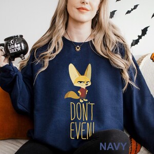 May include: Navy blue sweatshirt with a cartoon fox in a red vest and an angry expression. The words "DON'T EVEN!" are printed in yellow below the fox. The word "NAVY" is printed at the bottom of the sweatshirt.