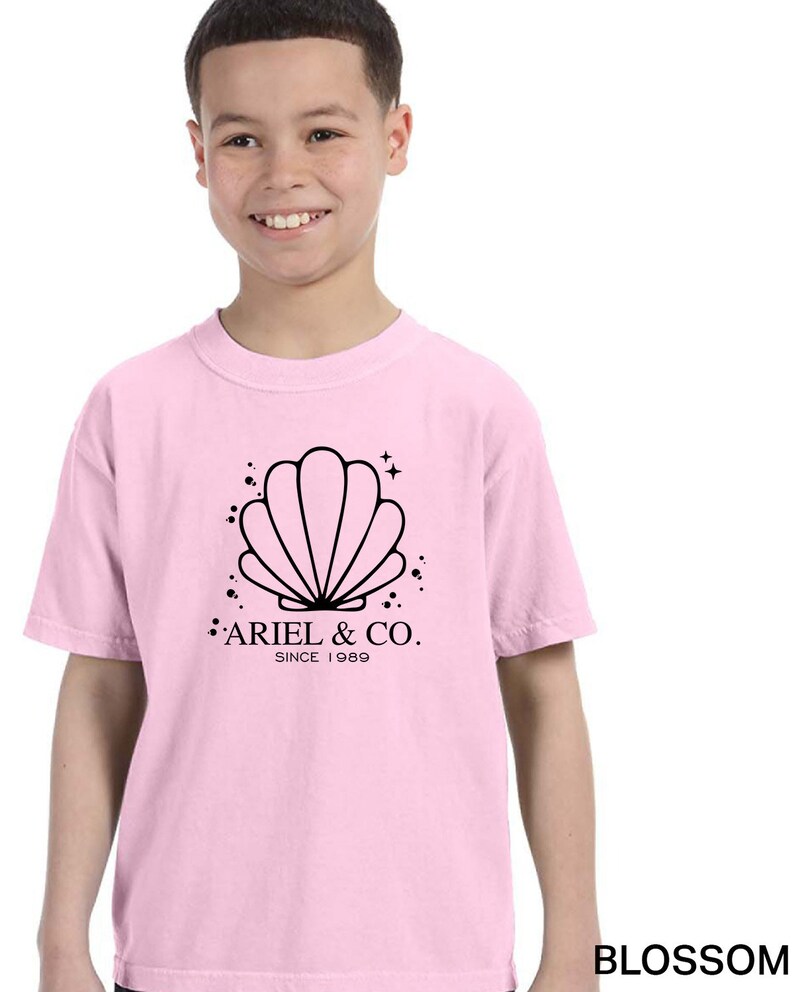 May include: Pink t-shirt with a black graphic of a seashell and the text "Ariel & Co. Since 1989"