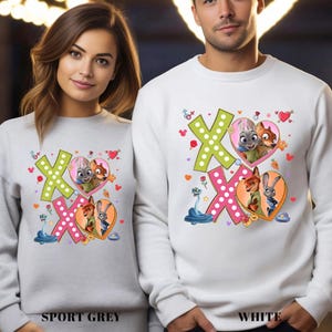 May include: Sport grey and white sweatshirts featuring a colorful graphic design. The design includes the letters "XO", hearts, and cartoon characters. The sweatshirts are a comfortable, casual style.