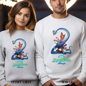 May include: Sport grey and white sweatshirts featuring a colorful graphic from the movie Zootopia 2. The design includes a blue snake wrapped around the characters Judy Hopps and Nick Wilde, with the movie title below.