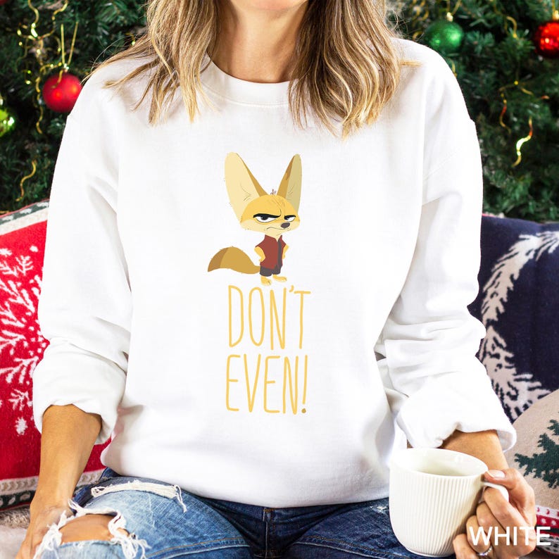 May include: White sweatshirt with a cartoon fennec fox in a red shirt and a stern expression. The yellow text "DON'T EVEN!" is printed below the fox. The sweatshirt is a casual style.