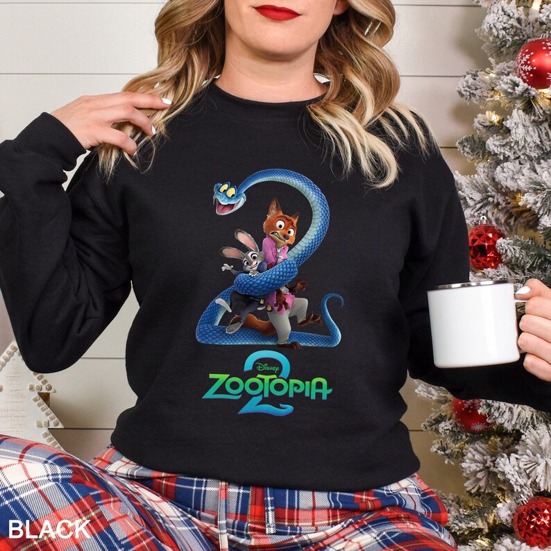 May include: Black sweatshirt featuring a graphic from the movie Zootopia 2. The design includes a blue snake wrapped around cartoon characters, with the movie title in teal. The word "BLACK" is printed at the bottom.