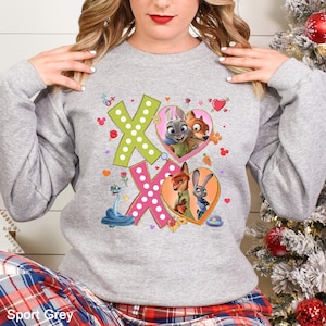 May include: Sport Grey sweatshirt featuring a colorful graphic with the text "XO" and images of characters from Zootopia. The design includes hearts, flowers, and cartoon characters. The sweatshirt is a light gray color.
