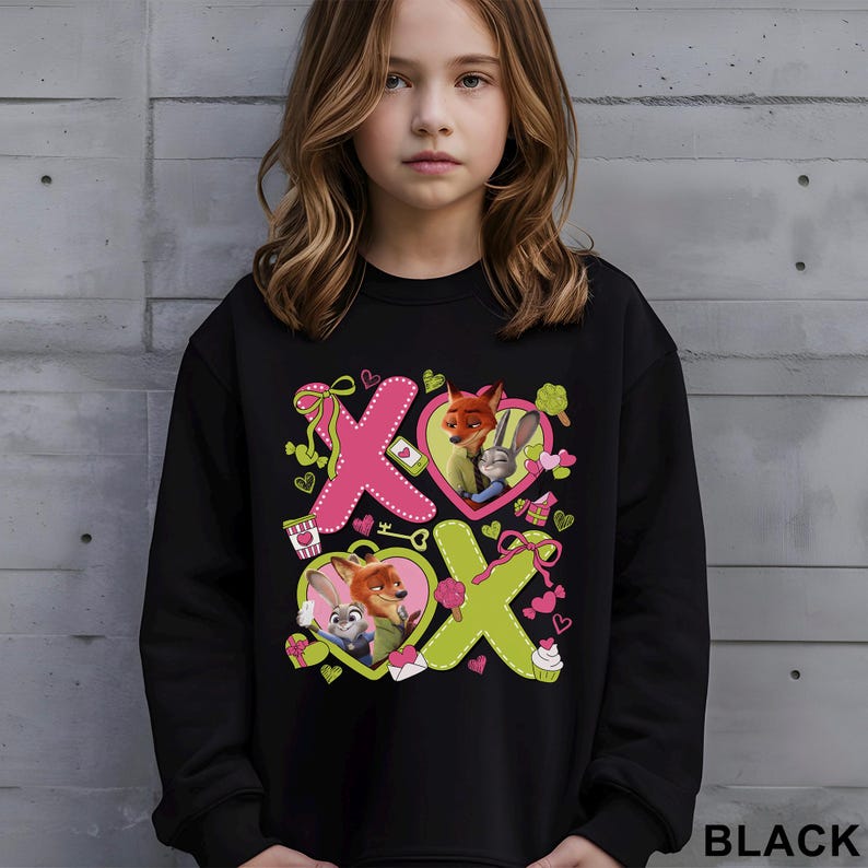 May include: Black sweatshirt featuring a colorful graphic of characters from the movie Zootopia. The design includes the letters "X" and "O" with heart-shaped frames, ribbons, and cupcakes. The word "BLACK" is printed at the bottom right.