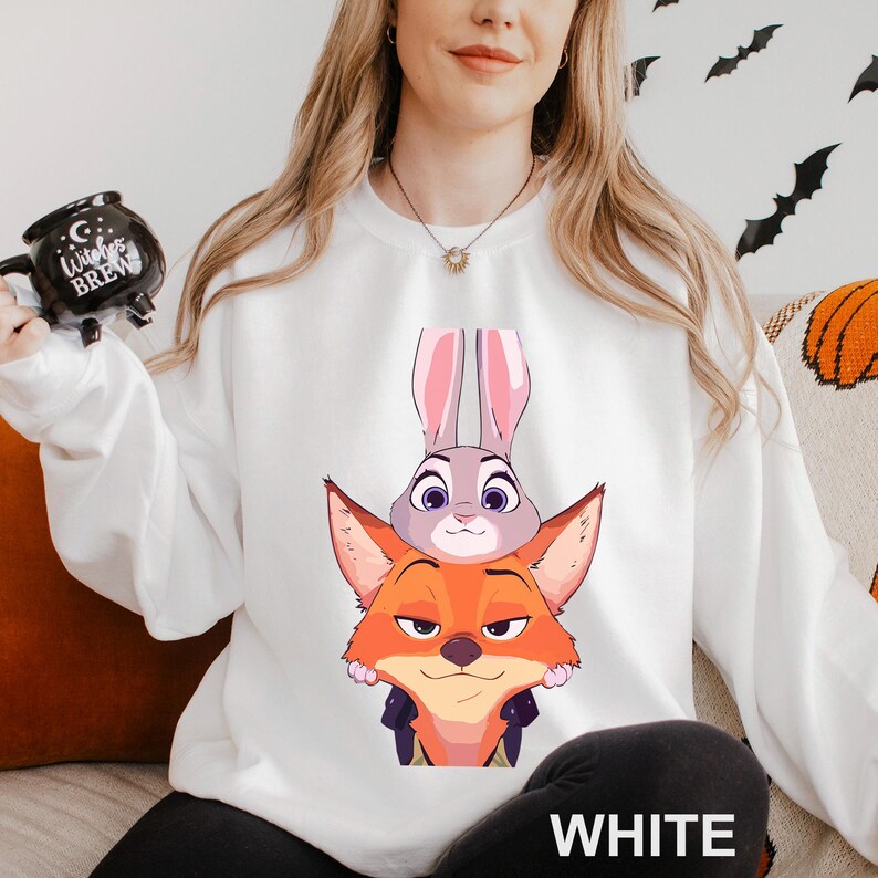 May include: White sweatshirt featuring a cartoon image of a fox and a bunny. The fox is orange and the bunny is gray. The word "WHITE" is printed in white at the bottom of the sweatshirt. The sweatshirt is long-sleeved.