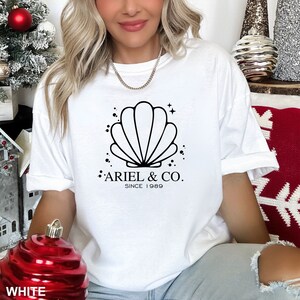 May include: White t-shirt with a black seashell graphic and the text "Ariel & Co. Since 1989".